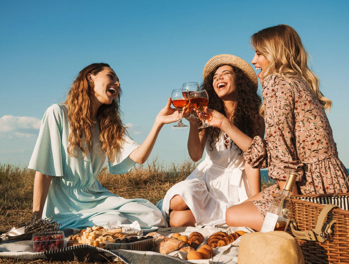 Amigas están sentadas de pic-nic y brindando con un vino ecológico rosado Gallego