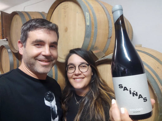 Jorge y Saleta con una botella de Secular puntuado por 18 puntos, por Jancis Robinson. Están en su bodega con barriles apilados al fondo.