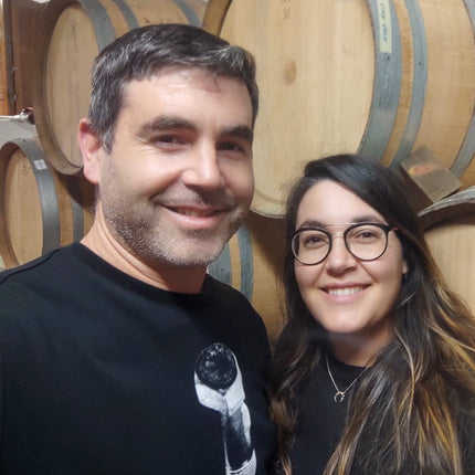 Retrato de Jorge y Saleta de bodegas Saiñas con barriles de vino como fondo, ambos están sonriendo..