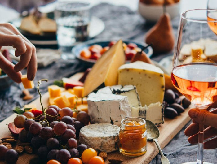 Amigos comiendo quesos Gallegos y con copas de vino naranja natural, en el centro está una tabla de quesos.