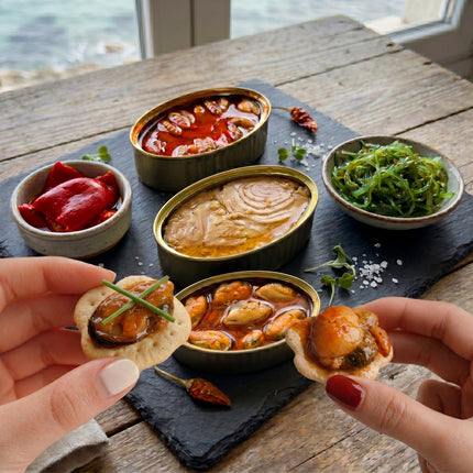 Pack de conservas gourmet de Vinnatura, se ven las manos de 2 chicas sosteniendo canapés de mejillones y zamburiñas