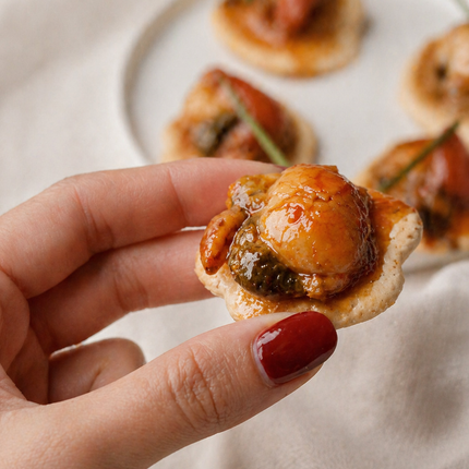 Canapé gourmet de zamburiña en salsa de vieira servido sobre galleta mariñeira