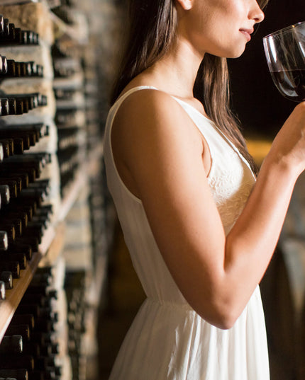 Una chica con un vestido blanco catando un vino tinto en el cellar de una bodega en Galicia