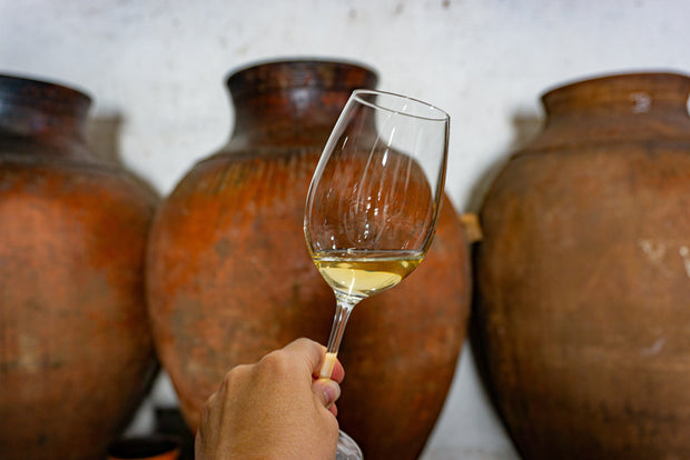 Tinajas de barro en una bodega Gallega con una copa de vino naranja natural.