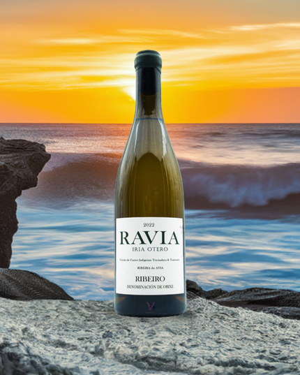 Vino ecológico Ravia 2022 de Iria Otero, sobre unas rocas en una puesta de sol, con el mar bravo con olas al fondo.