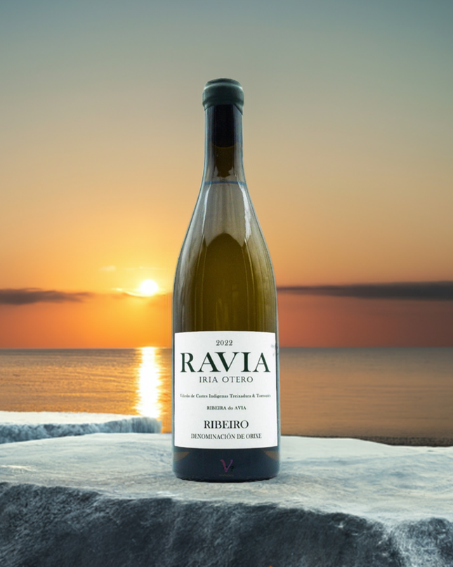 Vino ecológico Ravia 2022 de Iria Otero sobre unas rocas en una puesta de sol con el mar al fondo.