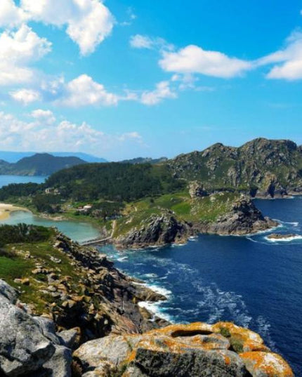 Vista aérea de las Islas Cíes en las Rías Baixas, mostrando un paisaje costero con aguas azules y acantilados rocosos bajo un cielo azul.