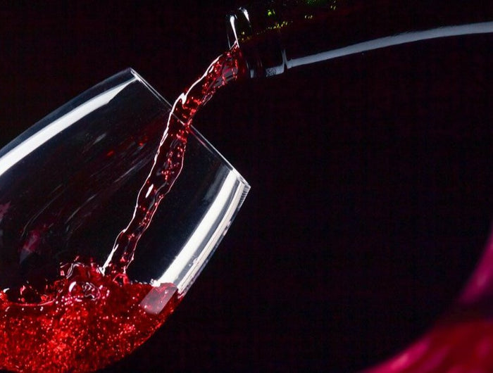 Sirviendo vino tinto en una copa sobre un fondo negro, y la representación del vino tinto al lado derecho de a imagen.