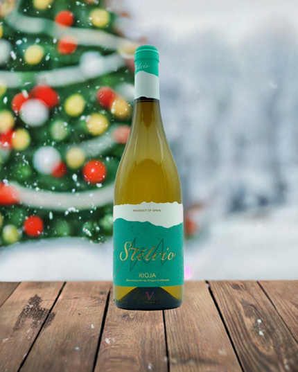 Vino blanco Malvasia sobre una mesa de madera y un árbol de navidad al fondo.