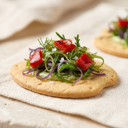 Tapa vegana con algas de Galicia, pimientos y brotes servida sobre galleta mariñeira como aperitivo gourmet