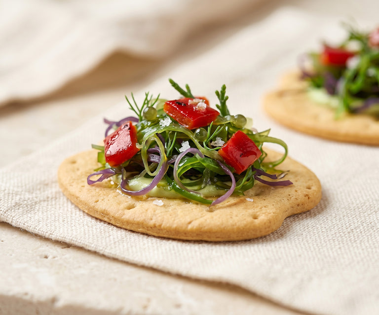 Tapa vegana con algas de Galicia, pimientos y brotes servida sobre galleta mariñeira como aperitivo gourmet