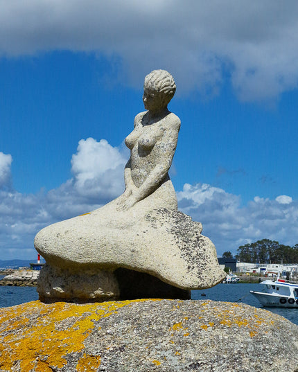 Sirena de piedra mirando al Océano Atlántico con los barcos mejilloneros al fondo