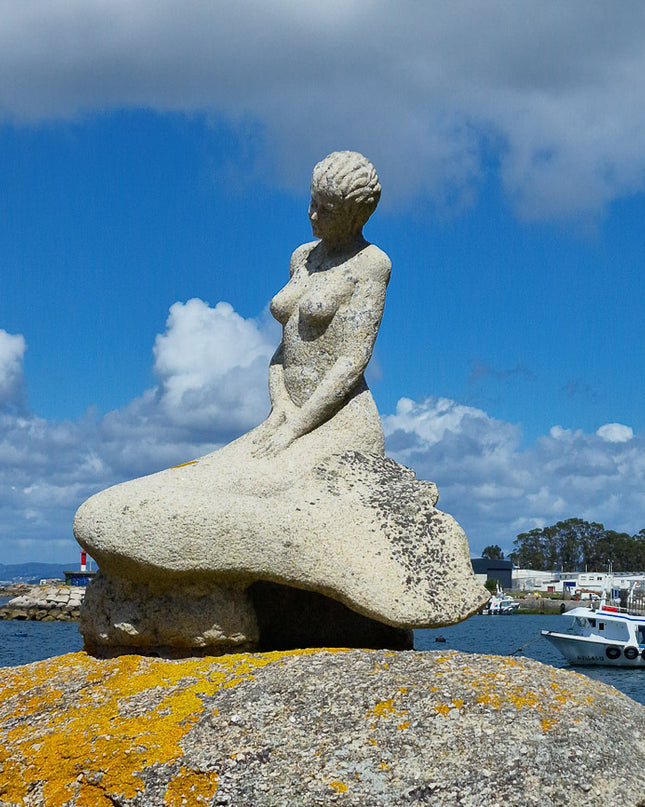 Sirena de piedra mirando al Océano Atlántico con los barcos mejilloneros al fondo