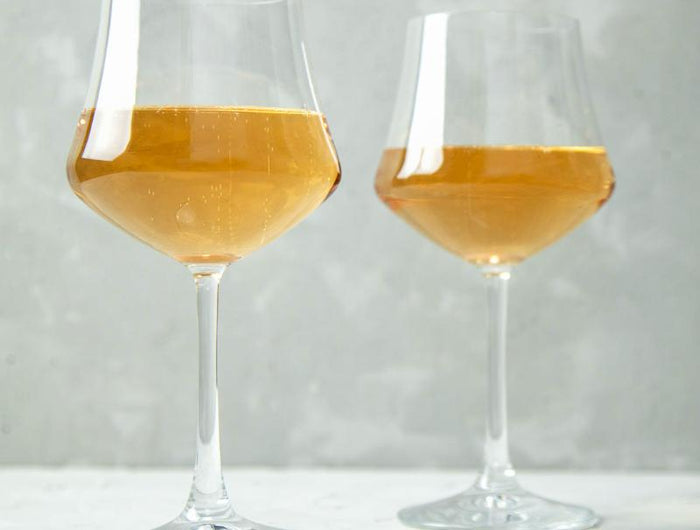 Dos copas de vino naranja sobre una mesa y un fondo blanco.