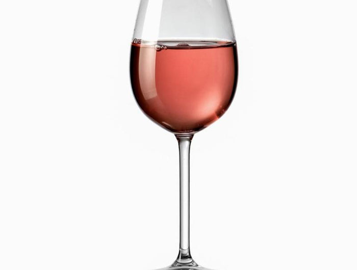 Copa de vino con vino rosado, con el reflejo de la base sobre un fondo blanco.