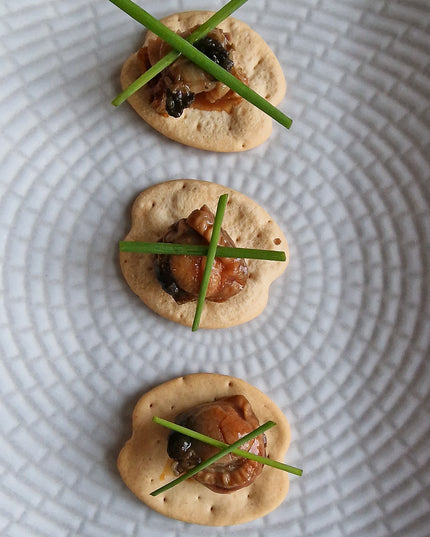 Una receta de canapés de zamburiñas sobre unas galletas mariñeiras con una decoración de cebollino en equis