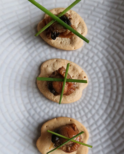 Una receta de canapés de zamburiñas sobre unas galletas mariñeiras con una decoración de cebollino en equis, un primer plano