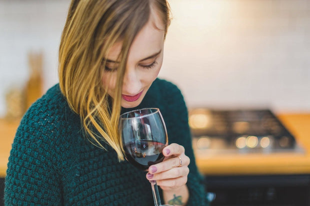 Mujer catando un vino tinto en una copa, disfrutando del aroma en un entorno acogedor.